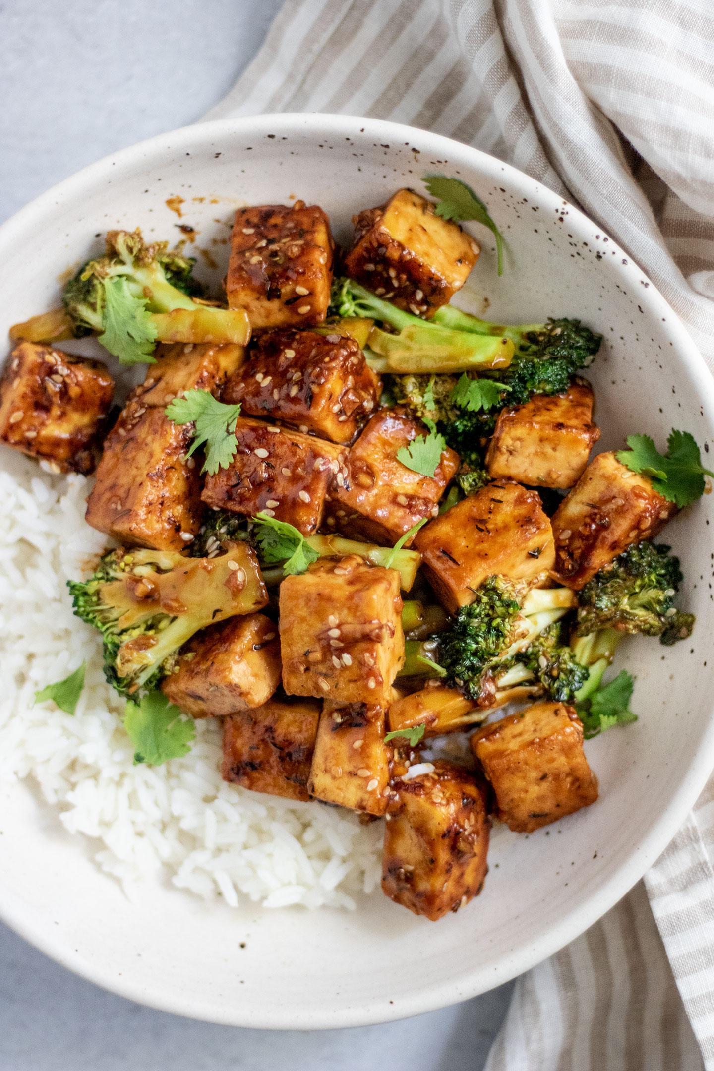 A person enjoying a bowl of crispy tofu and broccoli stir-fry