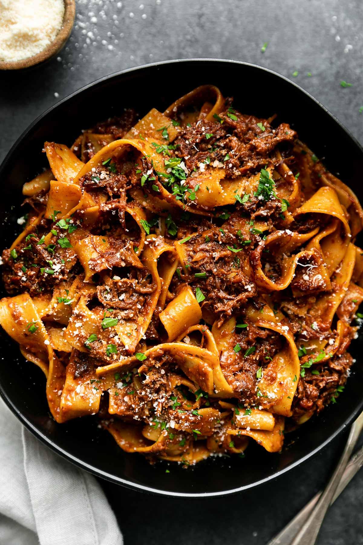 Close-up shot of tender short rib ragu served over pappardelle pasta with a sprinkle of vibrant gremolata