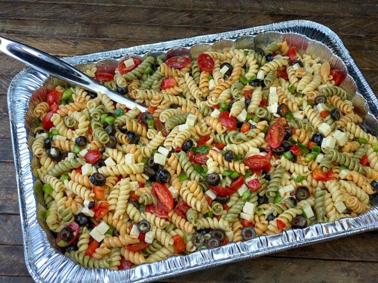 A person serving a large bowl of pasta salad at an outdoor party