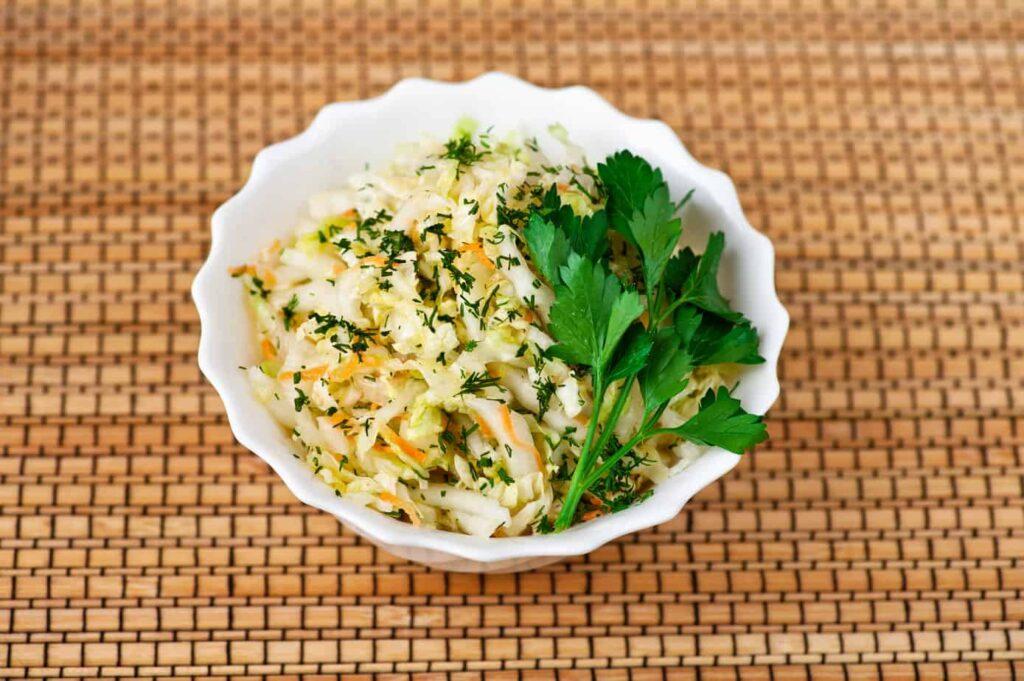 Overhead shot of a vibrant Sauerkraut and Glasswort Salad, drizzled with Olive Oil, in a white bowl.