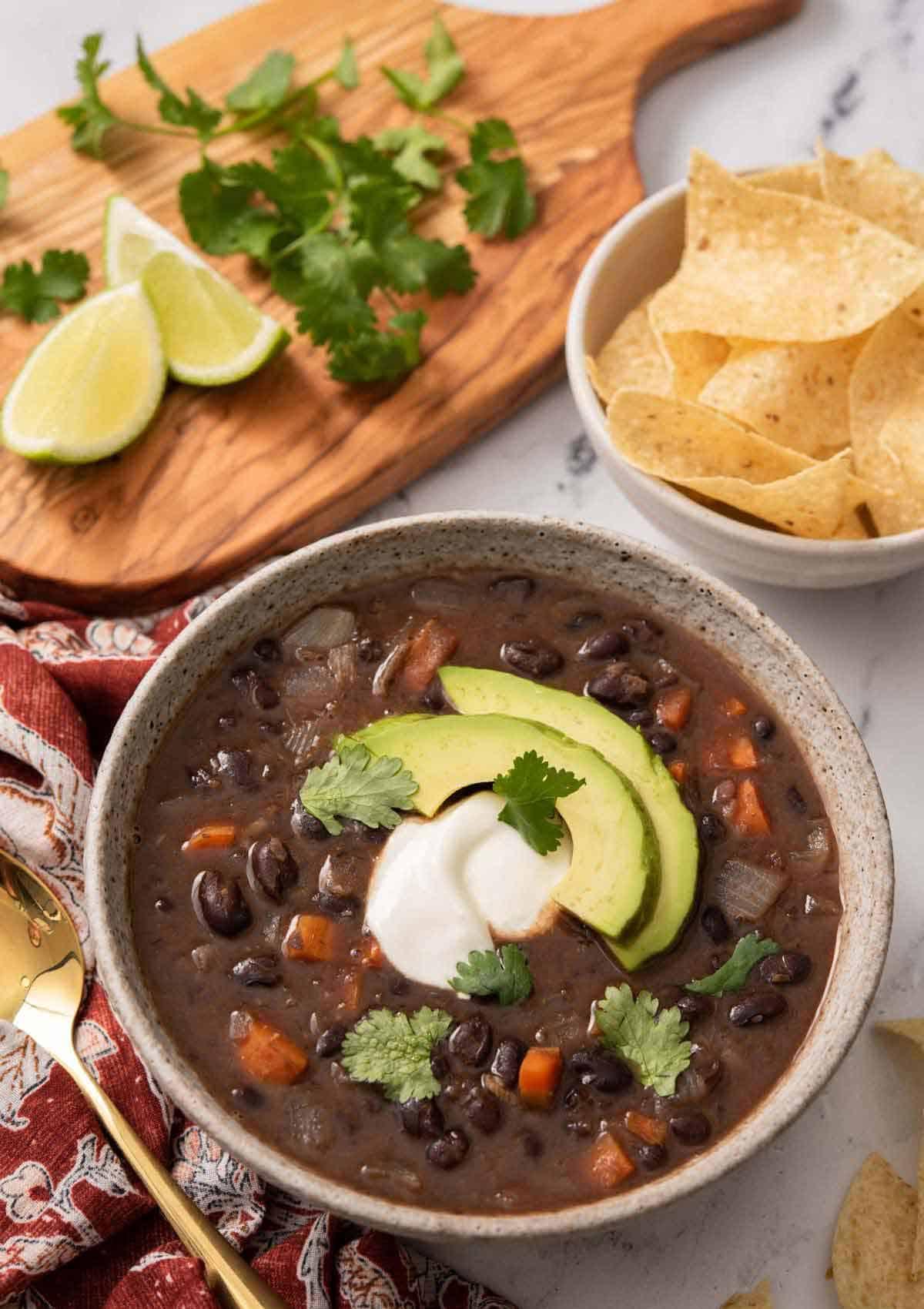 A bowl of spicy black bean soup topped with avocado, garnished with cilantro and a lime wedge