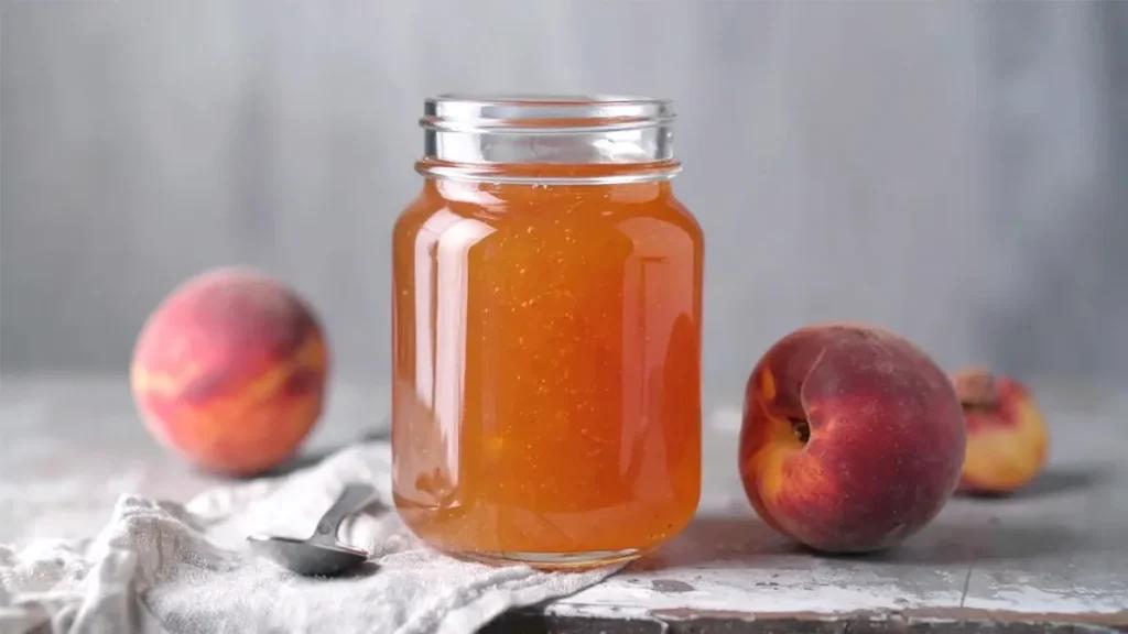 Canning jars filled with peach preserves cooling on a kitchen counter