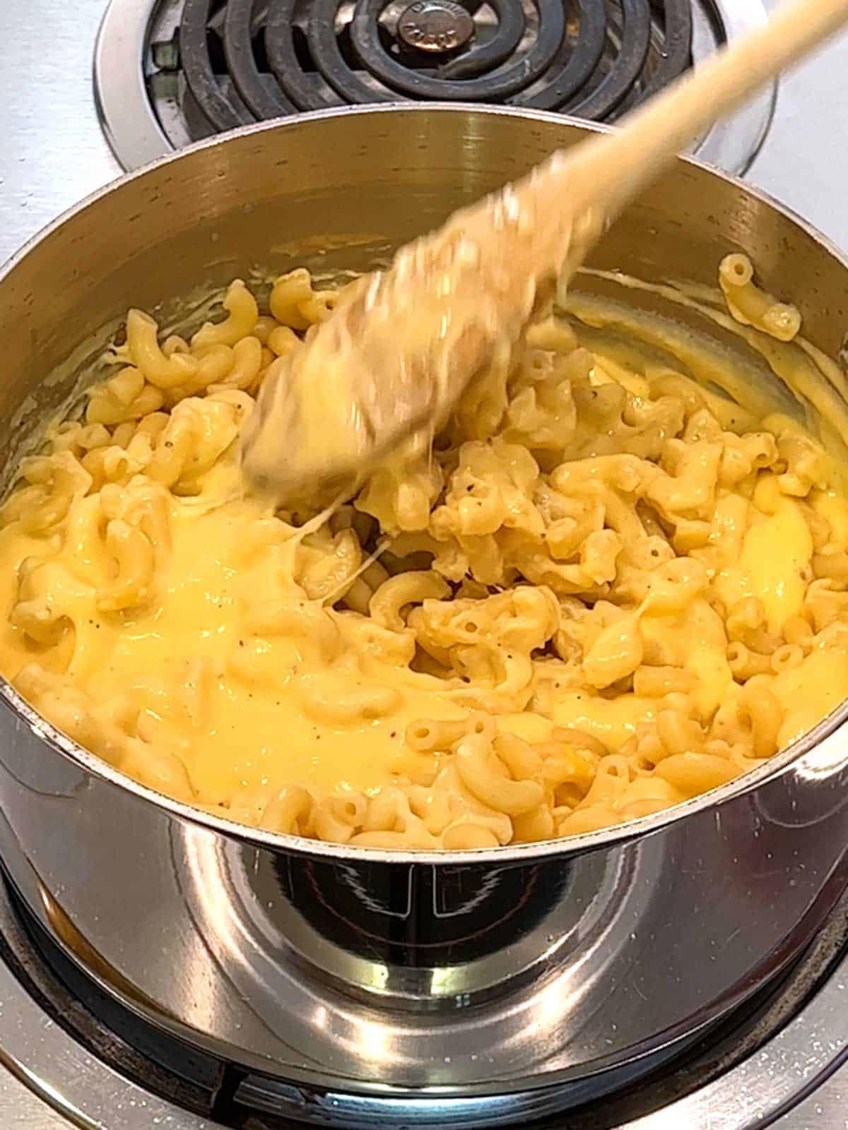 A person stirring a large pot of creamy mac and cheese
