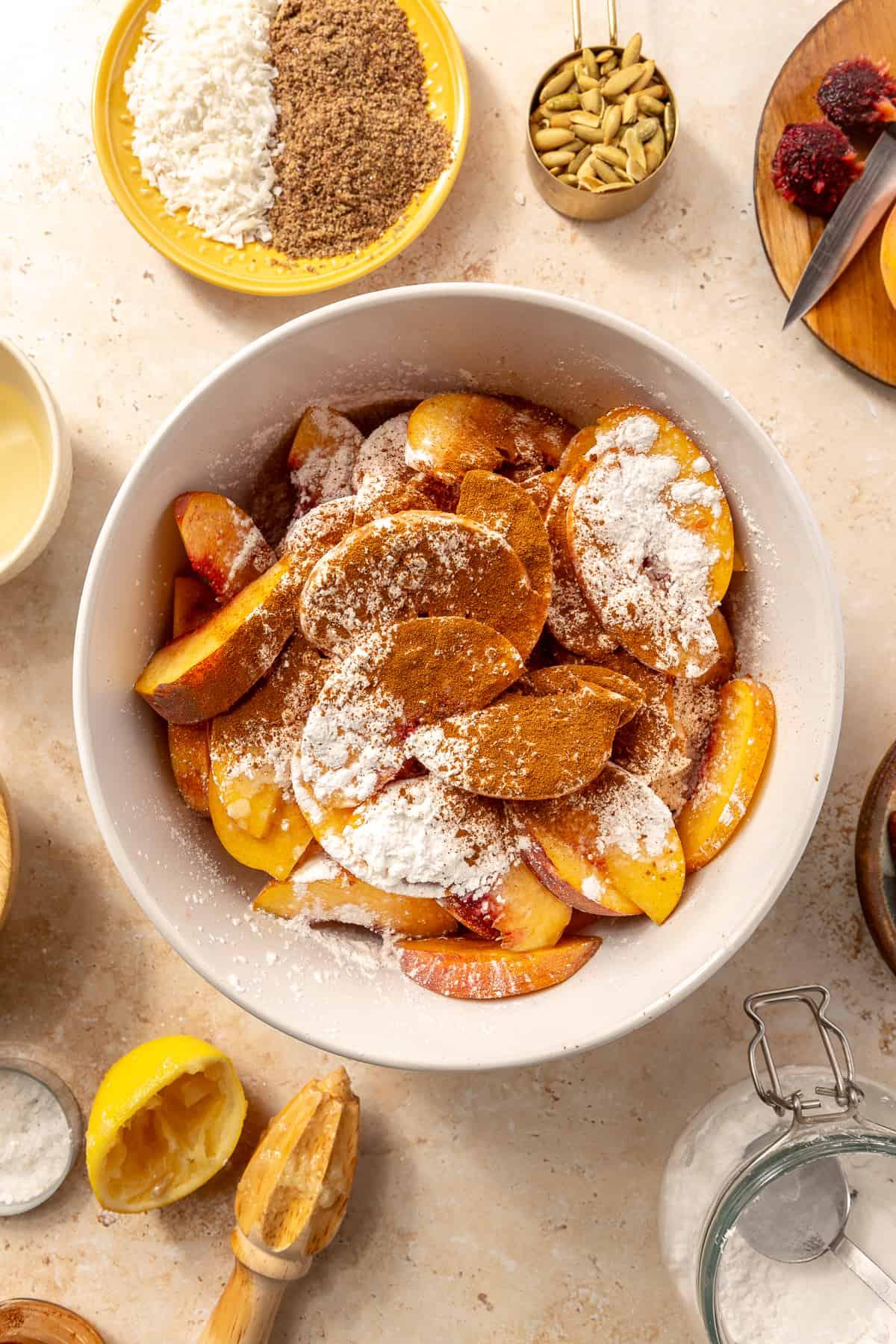 A rustic, golden-brown Paleo Peach Cobbler Fruit Bowl brimming with juicy peaches, topped with a crumble topping. The bowl is presented on a wooden table with a scattering of fresh peaches and mint leaves.