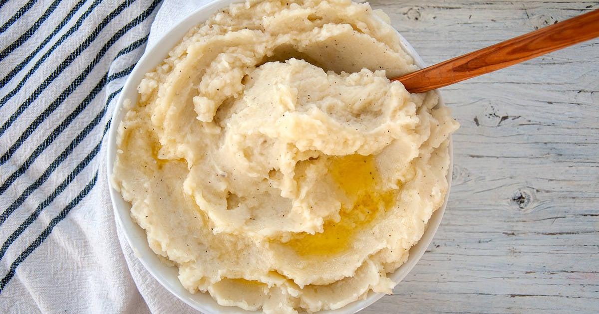 Close-up of fluffy mashed potatoes being stirred with a wooden spoon in a rustic white bowl, steam rising