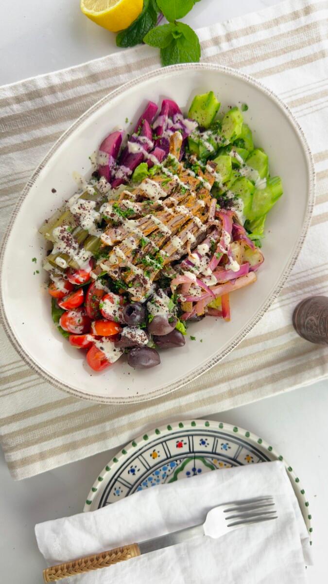 A platter of lamb shawarma and barley salad, garnished with fresh herbs and lemon wedges