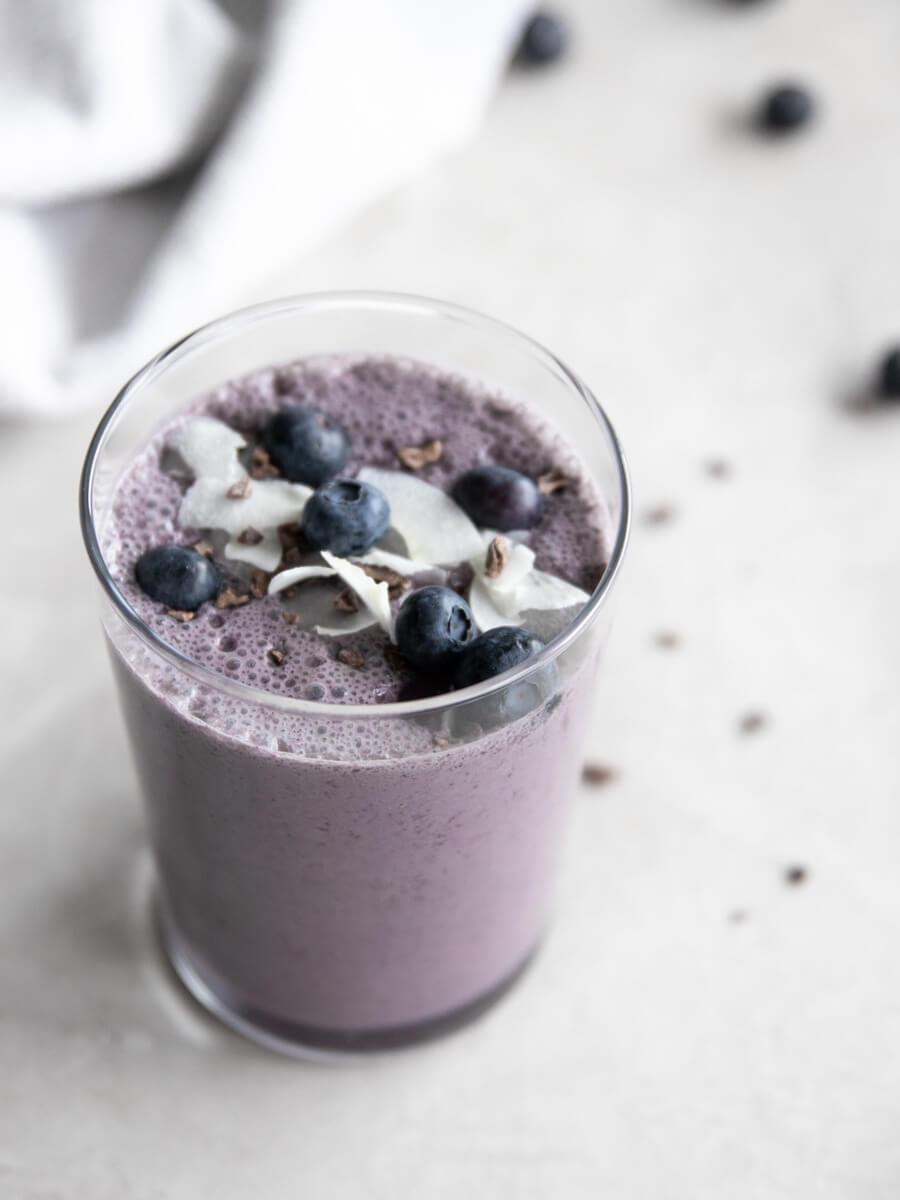 Close-up shot of a glass of blueberry coconut cream smoothie with fresh blueberries and coconut flakes on top