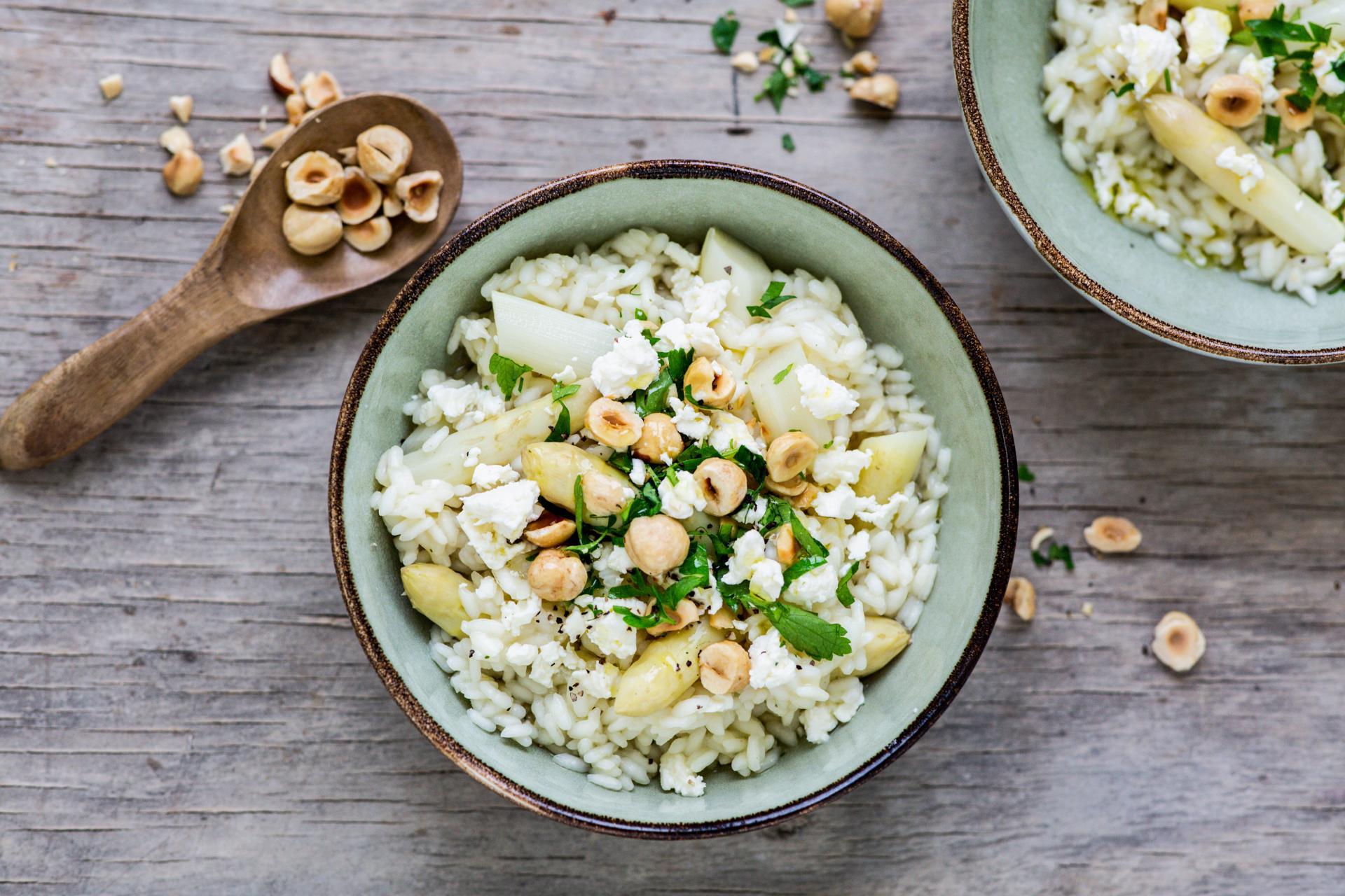 Person plating a bowl of asparagus risotto with feta