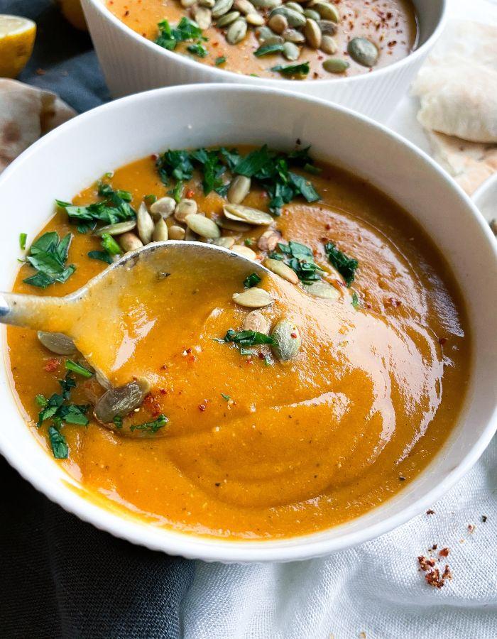 Close up of a bowl of creamy vegan lentil soup garnished with fresh herbs and lemon zest
