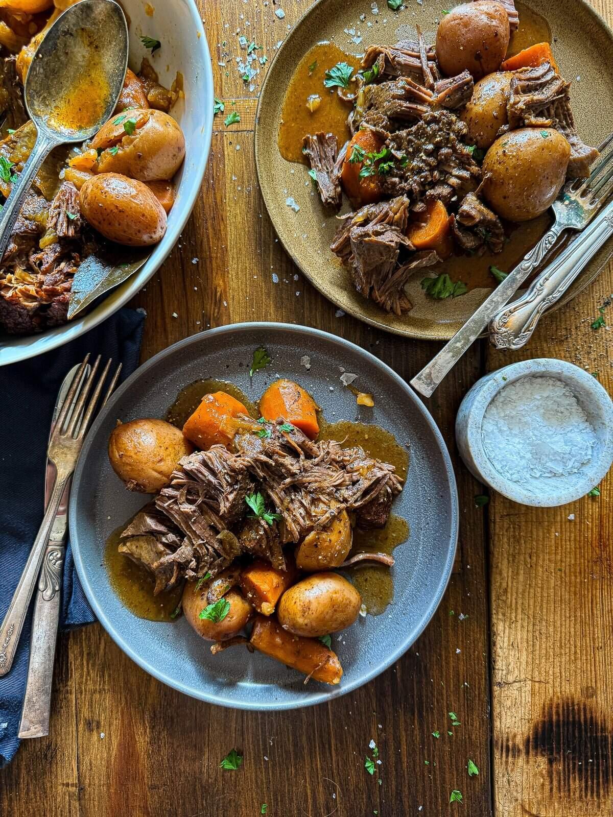 A rustic wooden table with a large roasting pan filled with perfectly roasted chicken and potatoes, alongside a bowl of cooked barley.  The scene is warmly lit, suggesting a cozy, home-cooked meal.