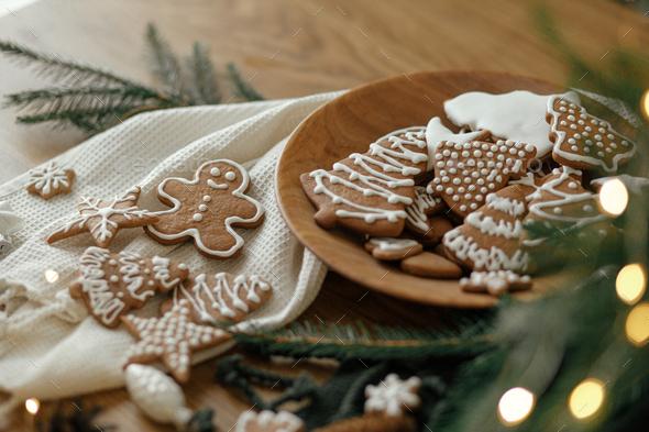A rustic wooden table with a plate of frosted fir gingerbread cookies, decorated with fir sprigs, surrounded by cozy holiday decorations.