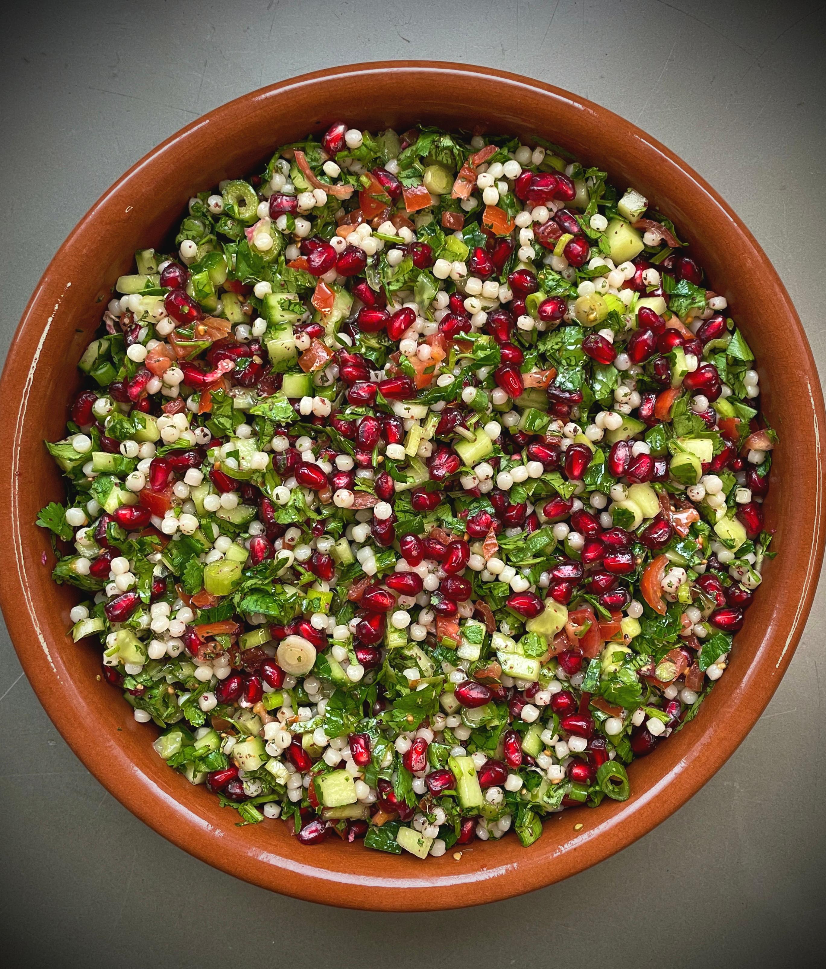 A rustic wooden table set with a platter of Tabbouleh Stuffed Tomatoes, accompanied by a bowl of olive oil, a lemon, and fresh herbs.