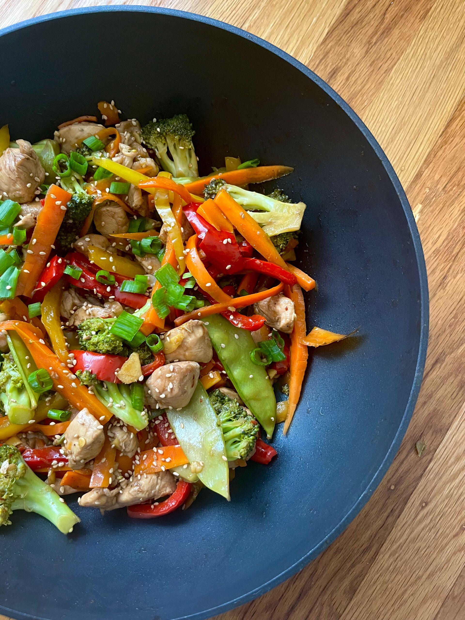 A colorful and vibrant chicken stir-fry protein bowl in a rustic setting