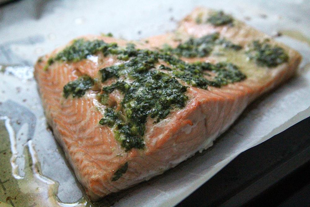 Close-up of a perfectly cooked basil-garlic salmon fillet on a baking sheet