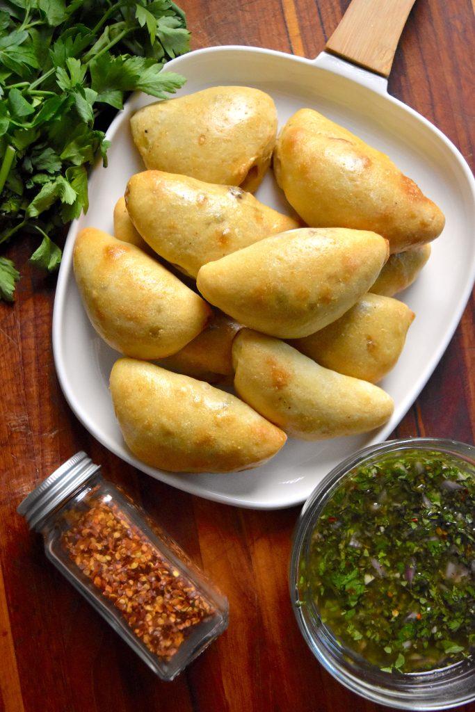 Close up shot of golden brown carne asada empanadas with vibrant green chimichurri sauce