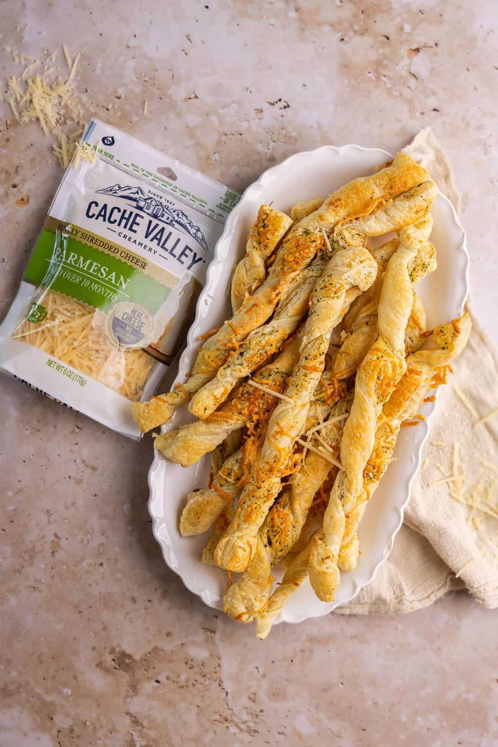 Golden savory parmesan puff pastry twists on a rustic wooden board, garnished with fresh herbs