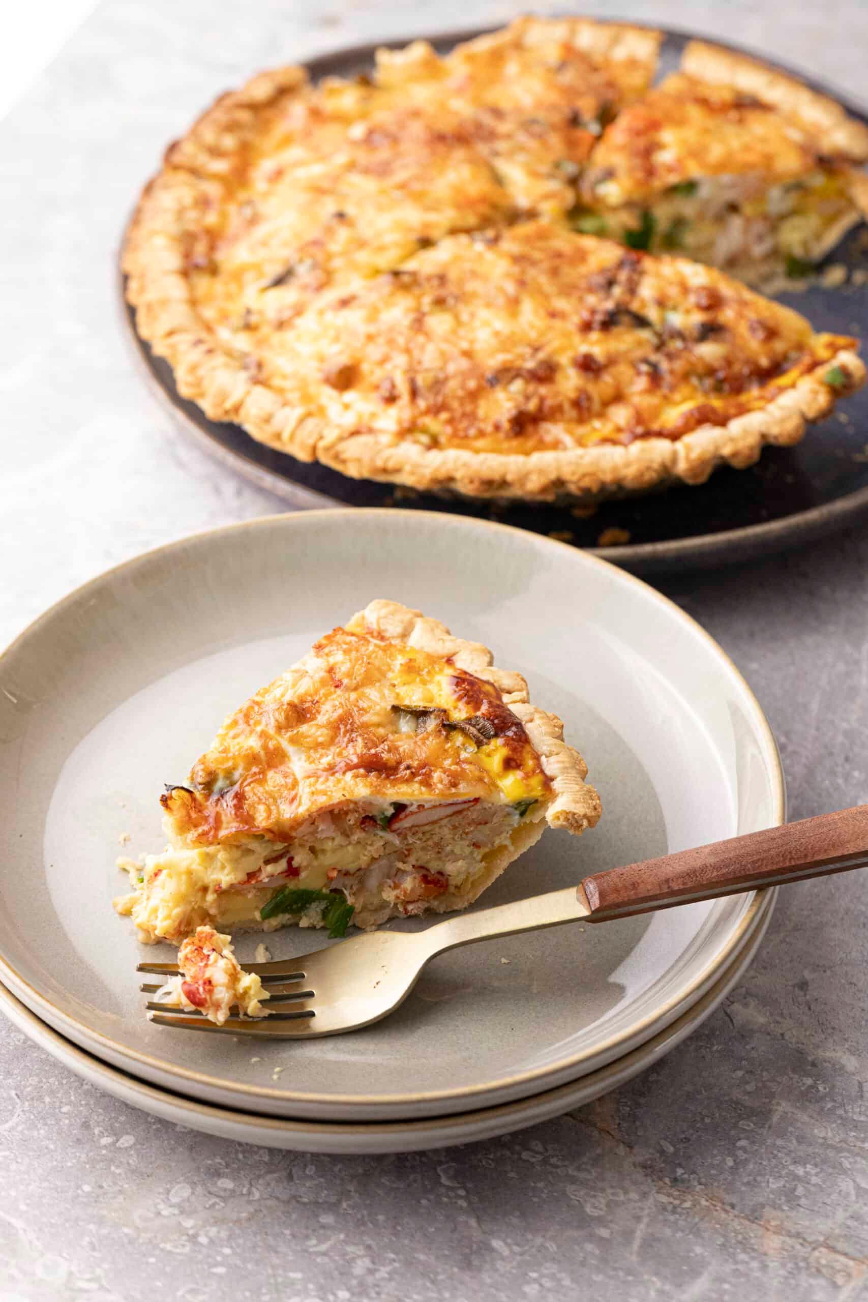 A golden-brown lobster and Gruyere tart on a white background, garnished with fresh herbs