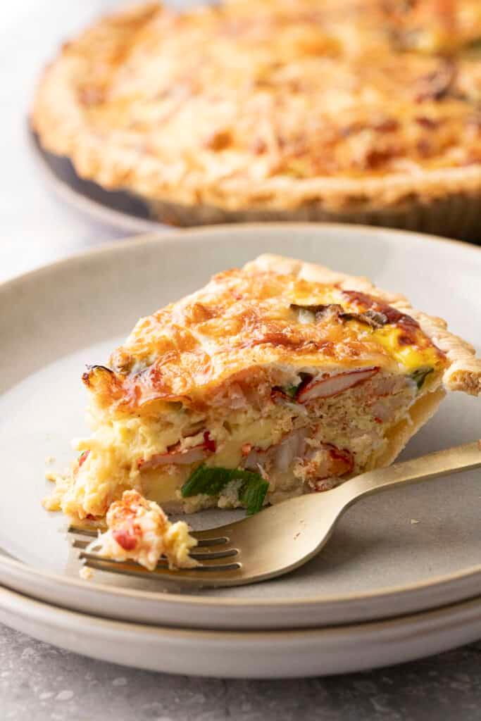 Close-up shot of a slice of lobster and chive quiche with lemon butter sauce, showing the flaky pastry crust and the creamy filling