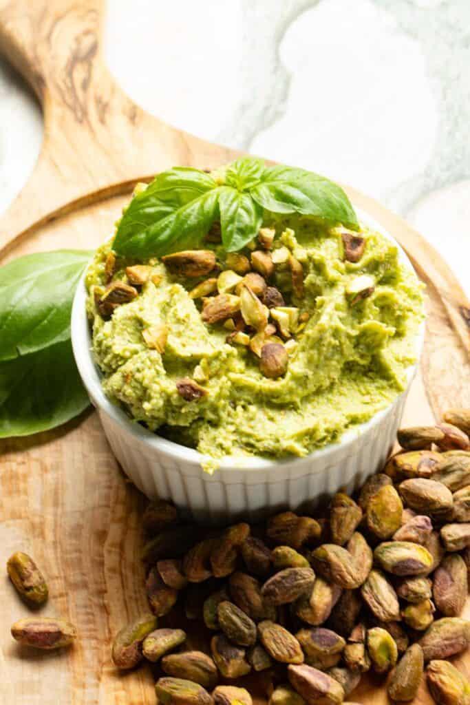 vibrant green basil and pistachio pesto in a bowl with fresh basil sprigs and pistachios