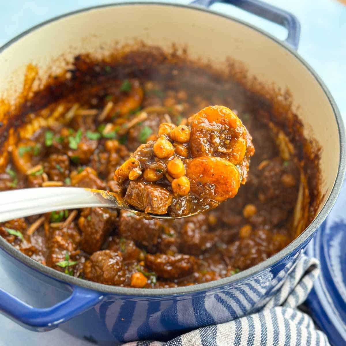 A rustic tagine pot filled with lamb, apricots, mint, and almonds, with steam rising.