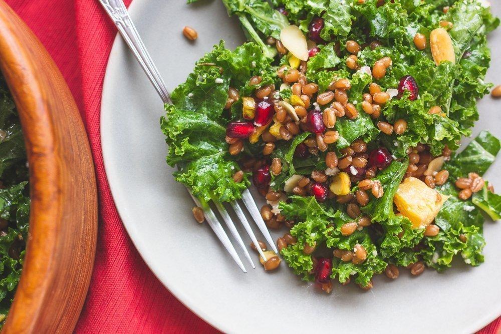 Vibrant photo of a wheat berry and kale salad with a lemon vinaigrette dressing drizzled over it.
