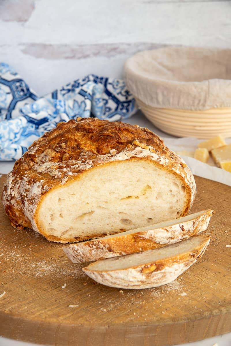 A loaf of Asiago wheat bread sliced and served on a wooden cutting board with drinks