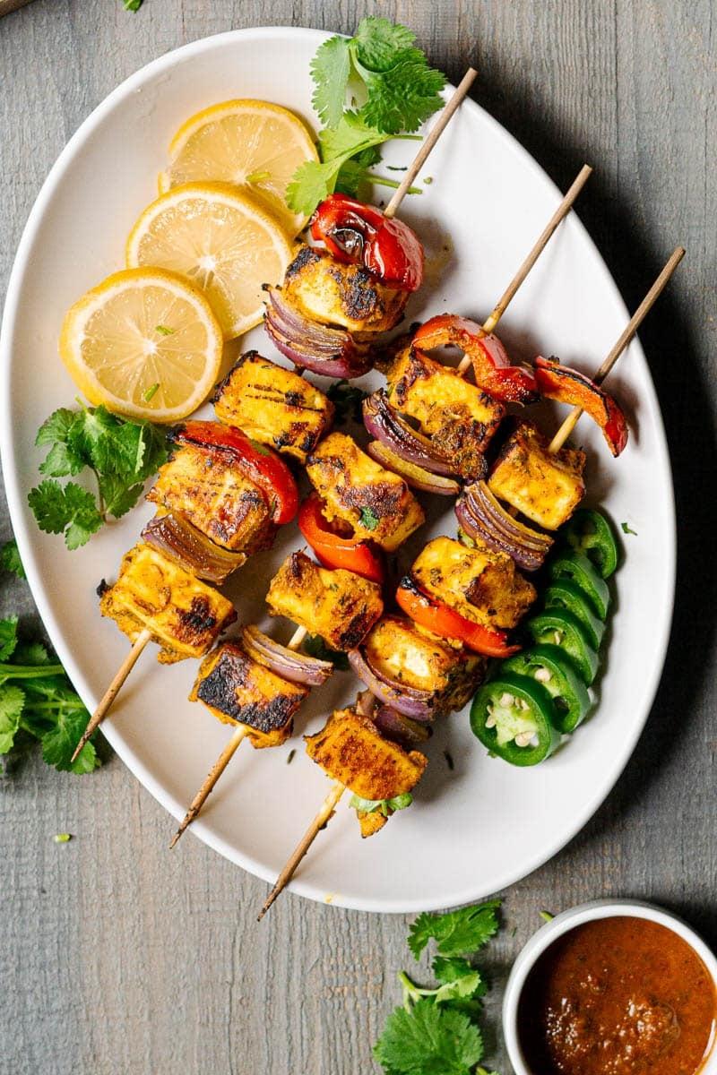 Finished Smoked Paneer Tikka Skewers garnished with cilantro and lemon wedges, plated beautifully
