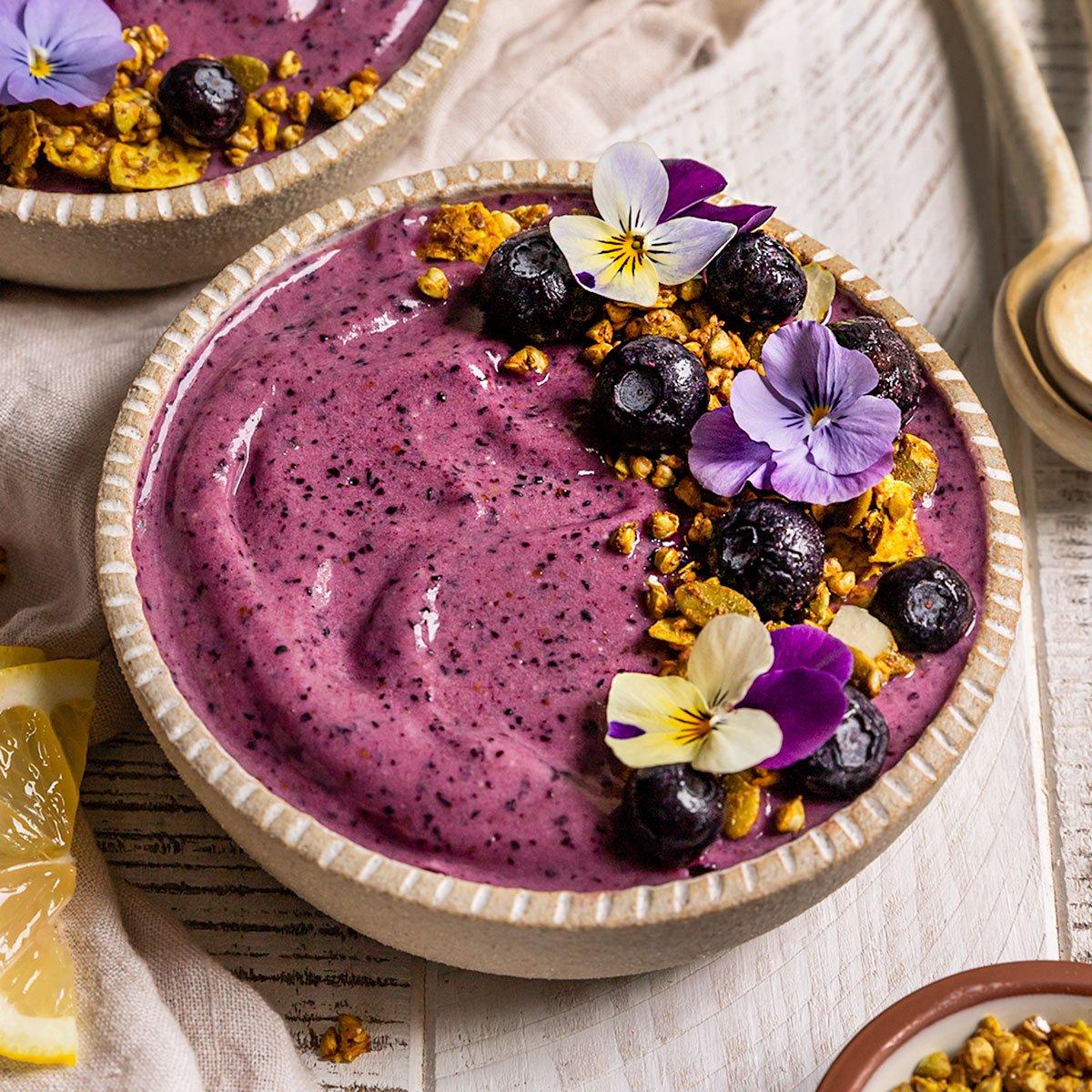 A vibrant and visually appealing blueberry lemon smoothie bowl topped with granola and fresh fruit, with a rustic background.