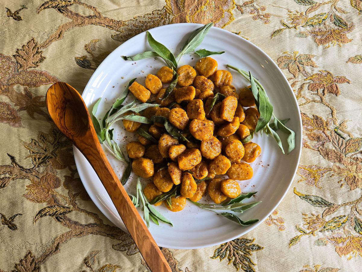 overhead view of several bowls of pumpkin gnocchi soup with brown sage butter, garnished with parmesan and sage