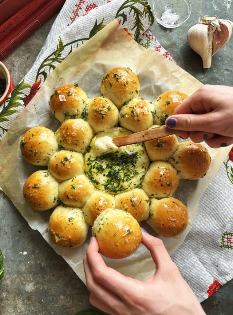 hands reaching for cheesy garlic bread bites on a rustic wooden board