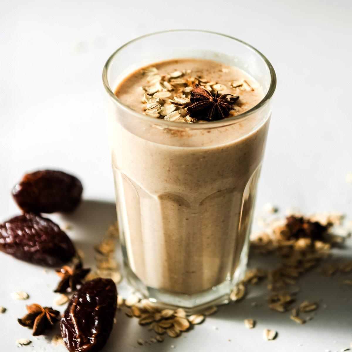 close up of a date and cinnamon smoothie in a glass with dates and cinnamon sticks scattered around