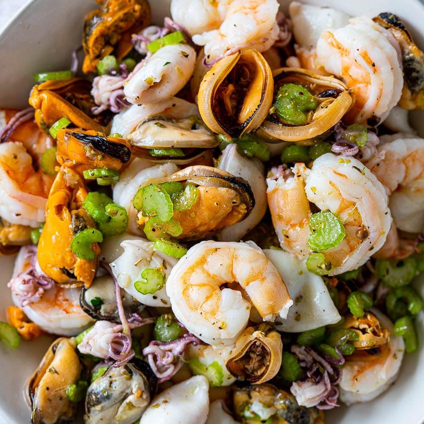 A selection of fresh seafood (shrimp, calamari, white fish) being marinated in a bowl with herbs and spices