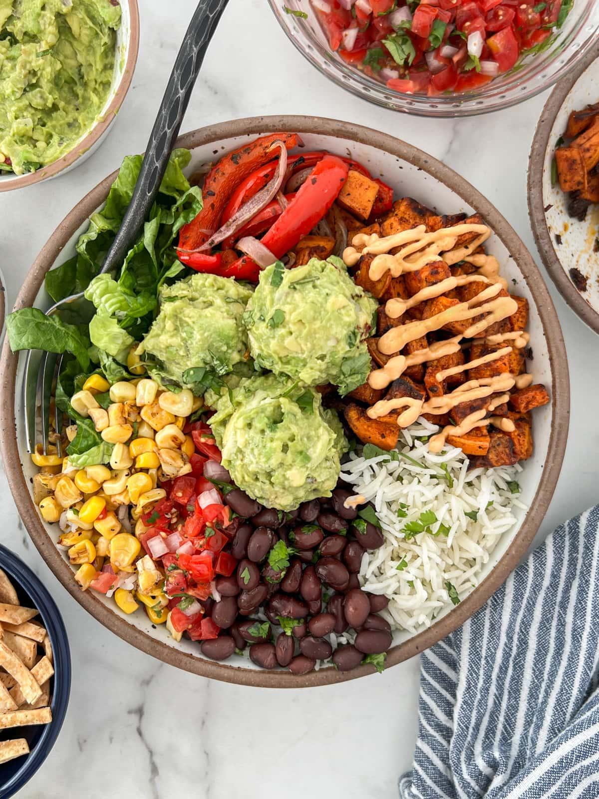 various toppings for black bean burrito bowls arranged on a table
