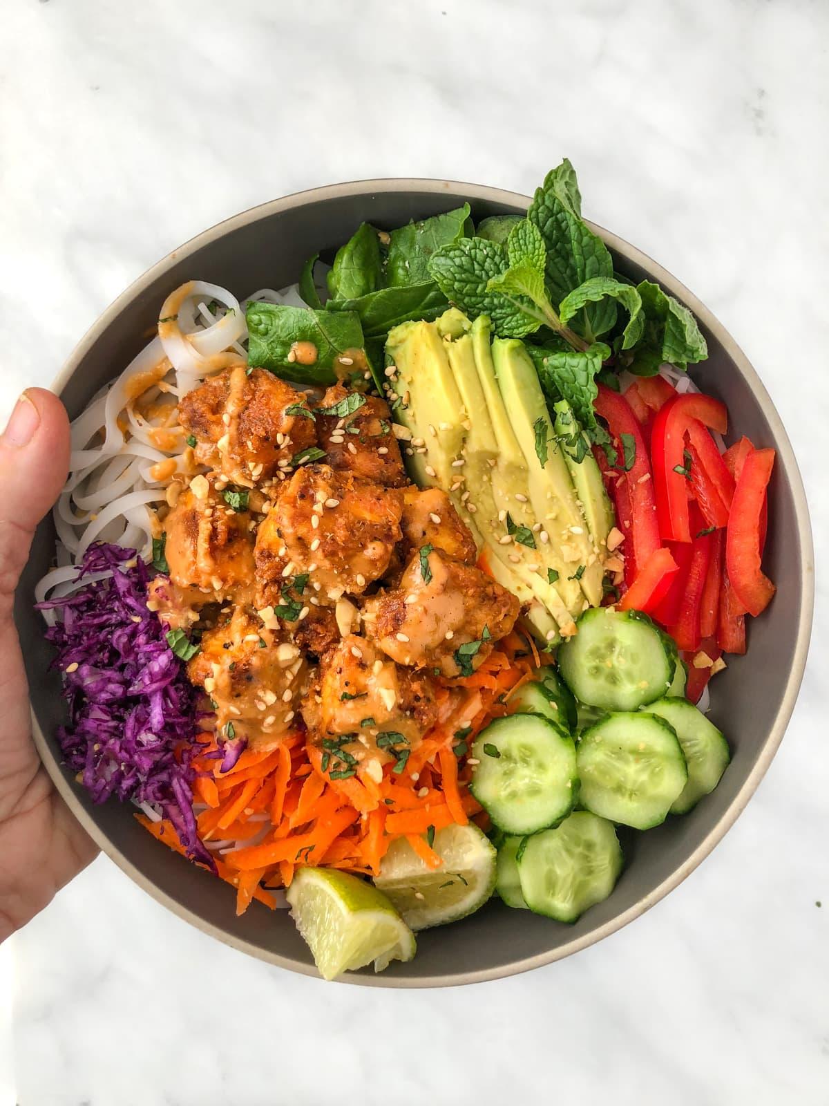 hands holding a spicy peanut noodles with tofu wrap