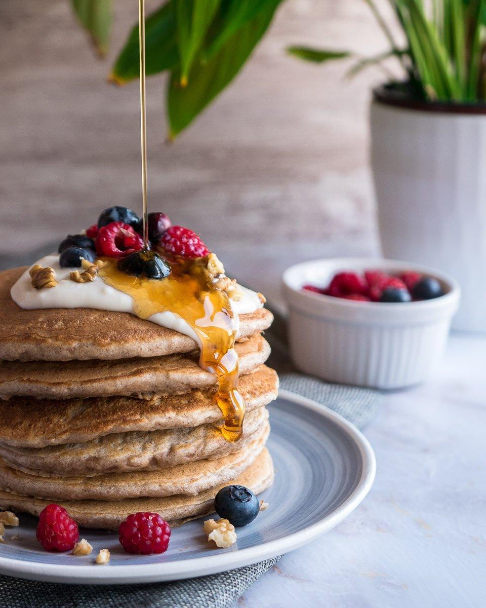 A stack of fluffy pear pancakes with a dusting of powdered sugar and a side of maple syrup, garnished with fresh pear slices and a sprinkle of ginger.