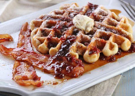 stack of lingonberry-maple syrup waffles topped with fresh lingonberries and a drizzle of syrup