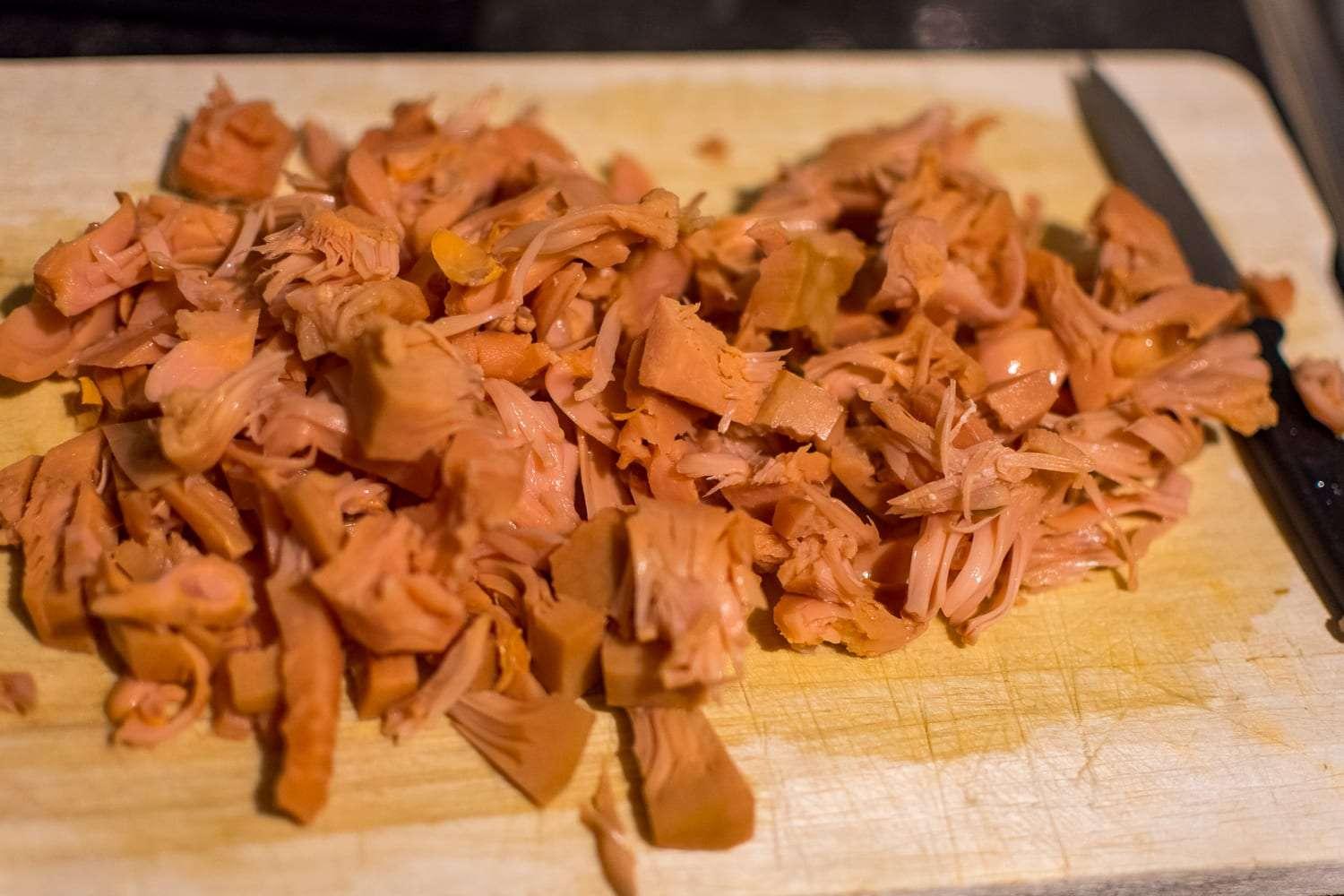 jackfruit being shredded with two forks on a wooden cutting board