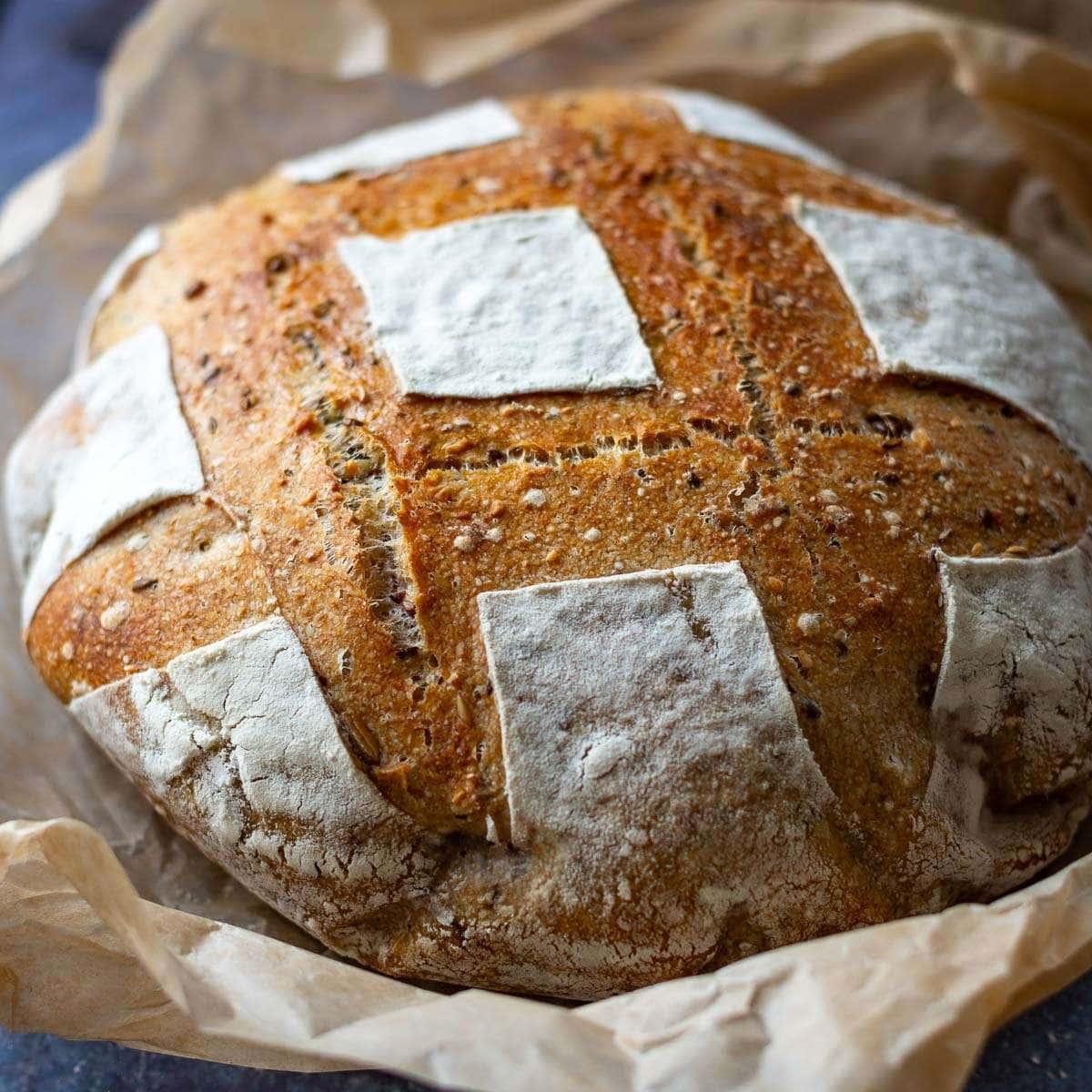 A loaf of rustic sourdough seeded bread, golden brown and crusty, with seeds scattered on top.