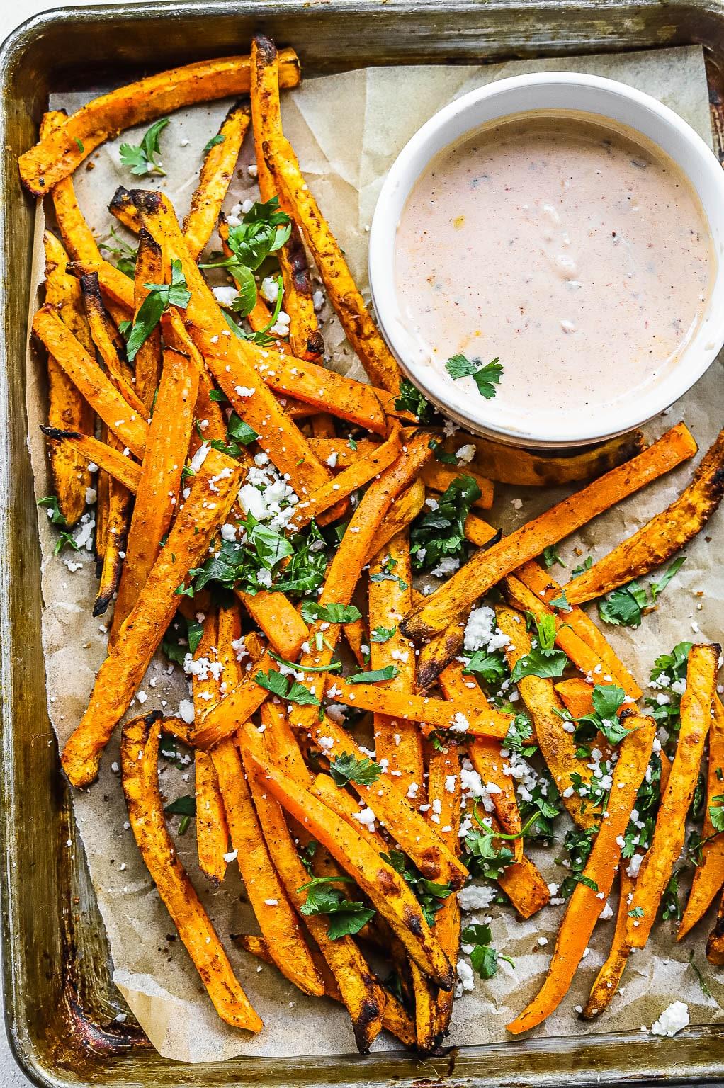 A serving of tempura sweet potato fries with chipotle ketchup, garnished with fresh herbs