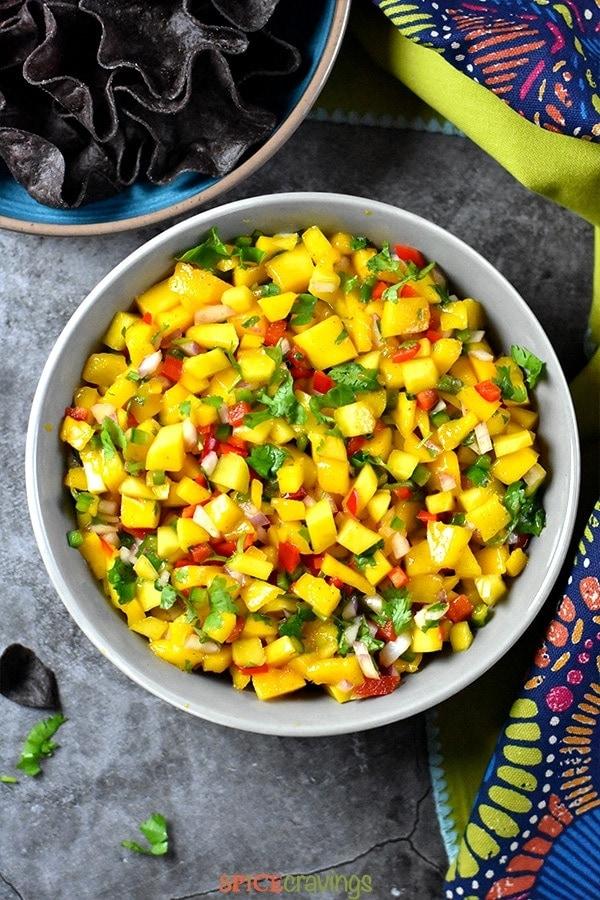 A vibrant bowl of mango salsa with fresh cilantro and red onion, garnished with lime wedges