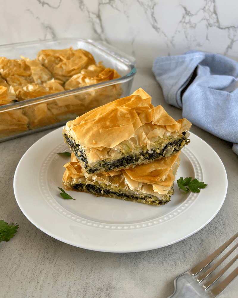 Golden brown, flaky spanakopita pastry with spinach filling, served on a white plate