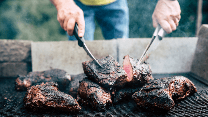 A person grilling a tri-tip steak on a barbecue
