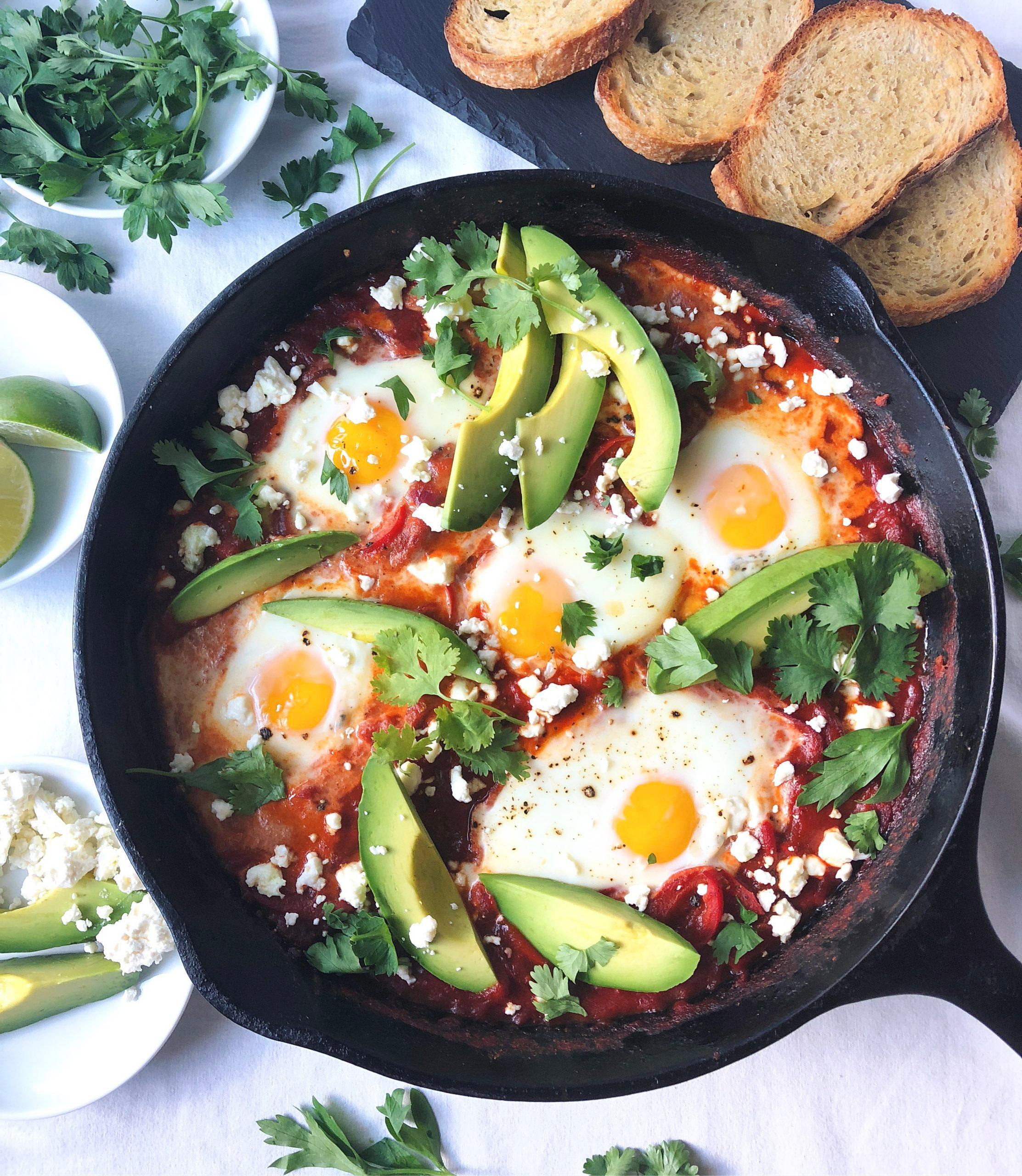 A close-up shot of a plate of shakshuka with a side of fresh green salad, garnished with feta cheese and herbs.