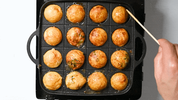 A colourful, well-lit shot of a tray of sizzling takoyaki balls being turned in a takoyaki pan