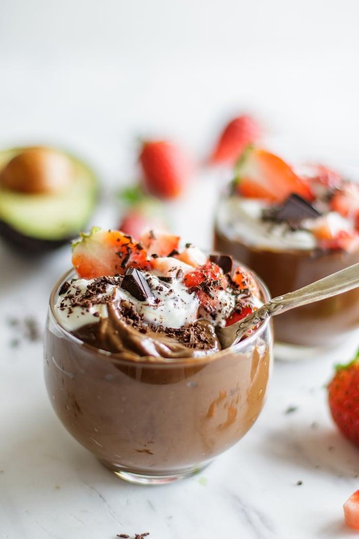 Hemp seed avocado chocolate mousse in glass bowls, garnished with berries and cocoa powder