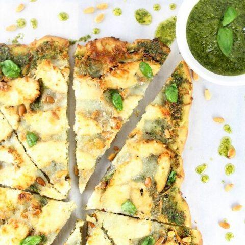 A person happily eating a slice of four-cheese curry pizza with pesto