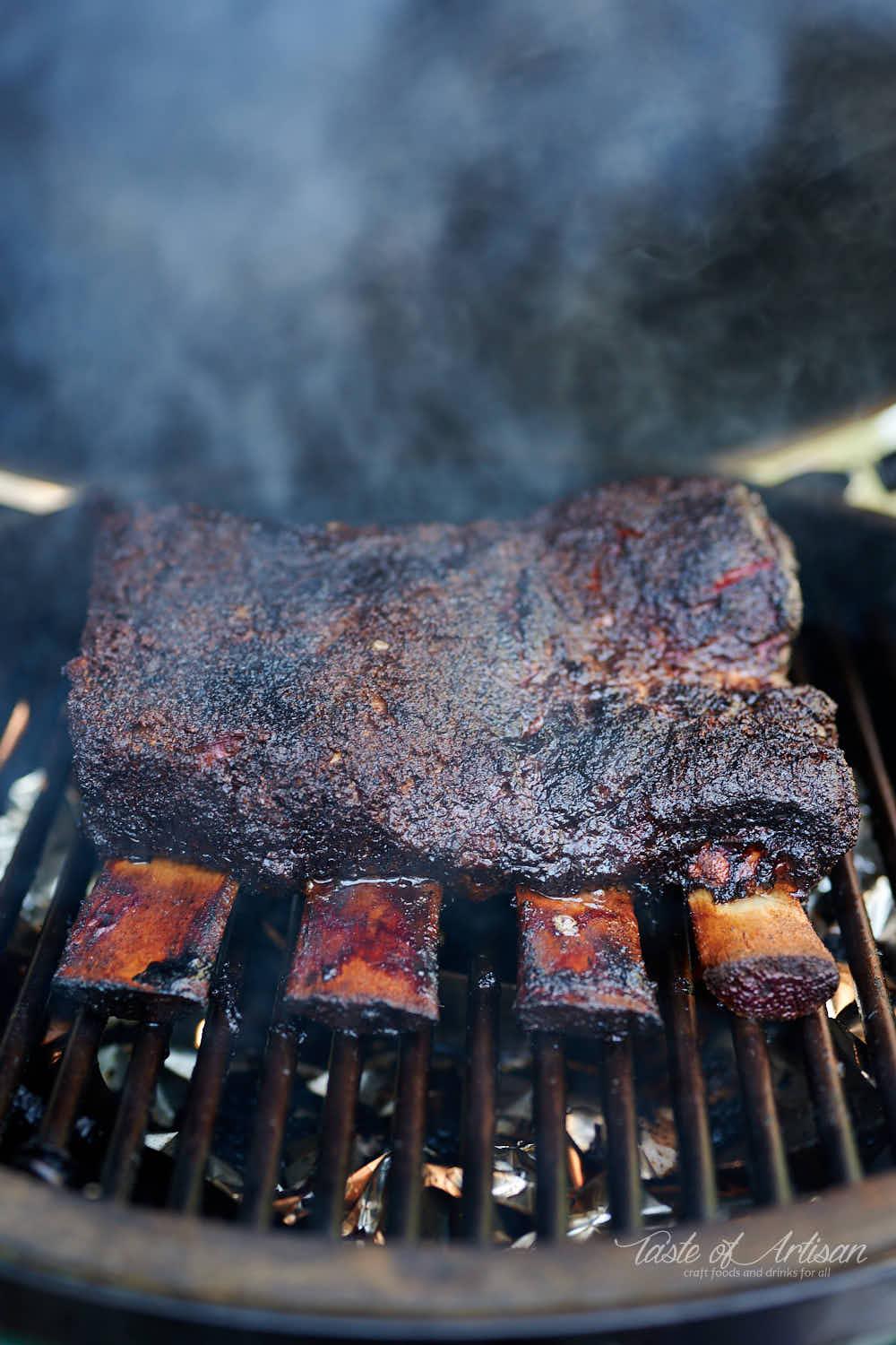 A smoker filled with beef ribs, with smoke billowing out