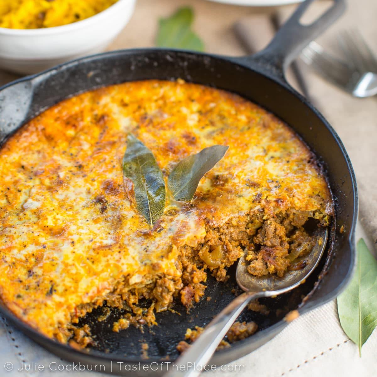 A beautifully presented Bobotie casserole in a baking dish, garnished with fried onions