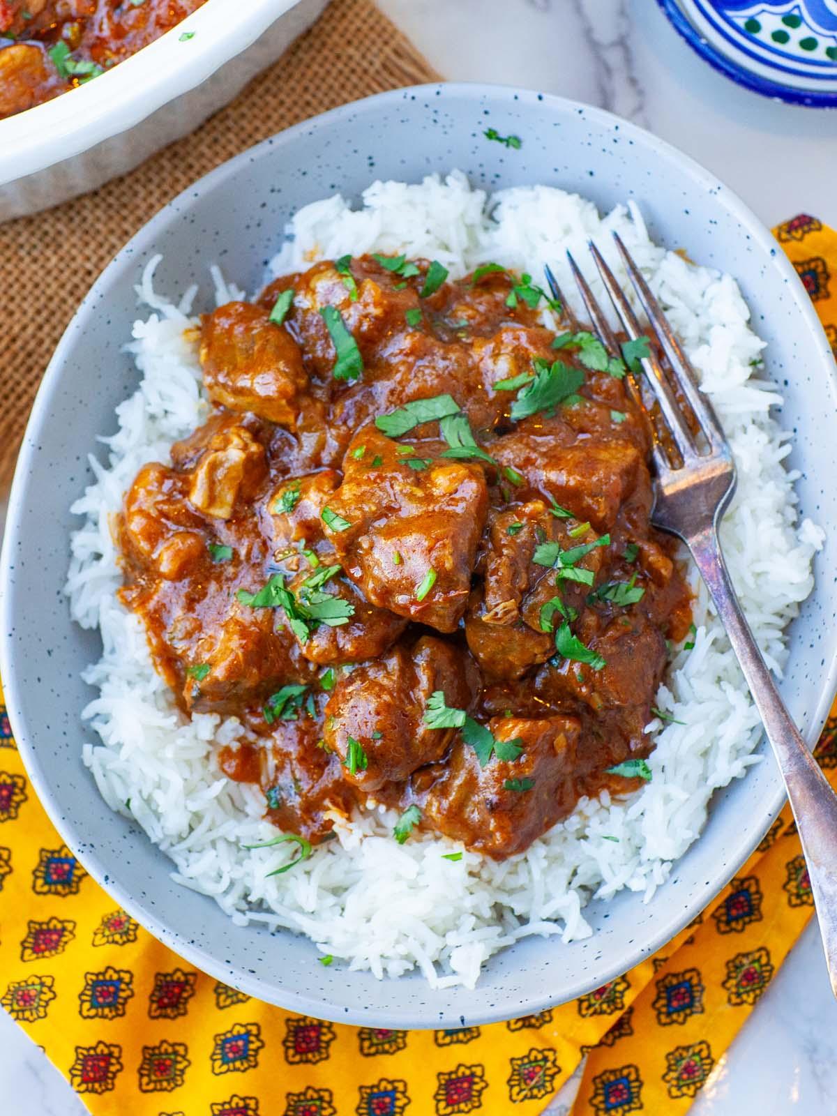 close-up of lamb curry with coconut milk and spinach being served over rice