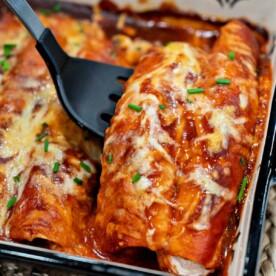 Close-up of a golden brown enchilada, cut in half to show the chicken and cheese filling